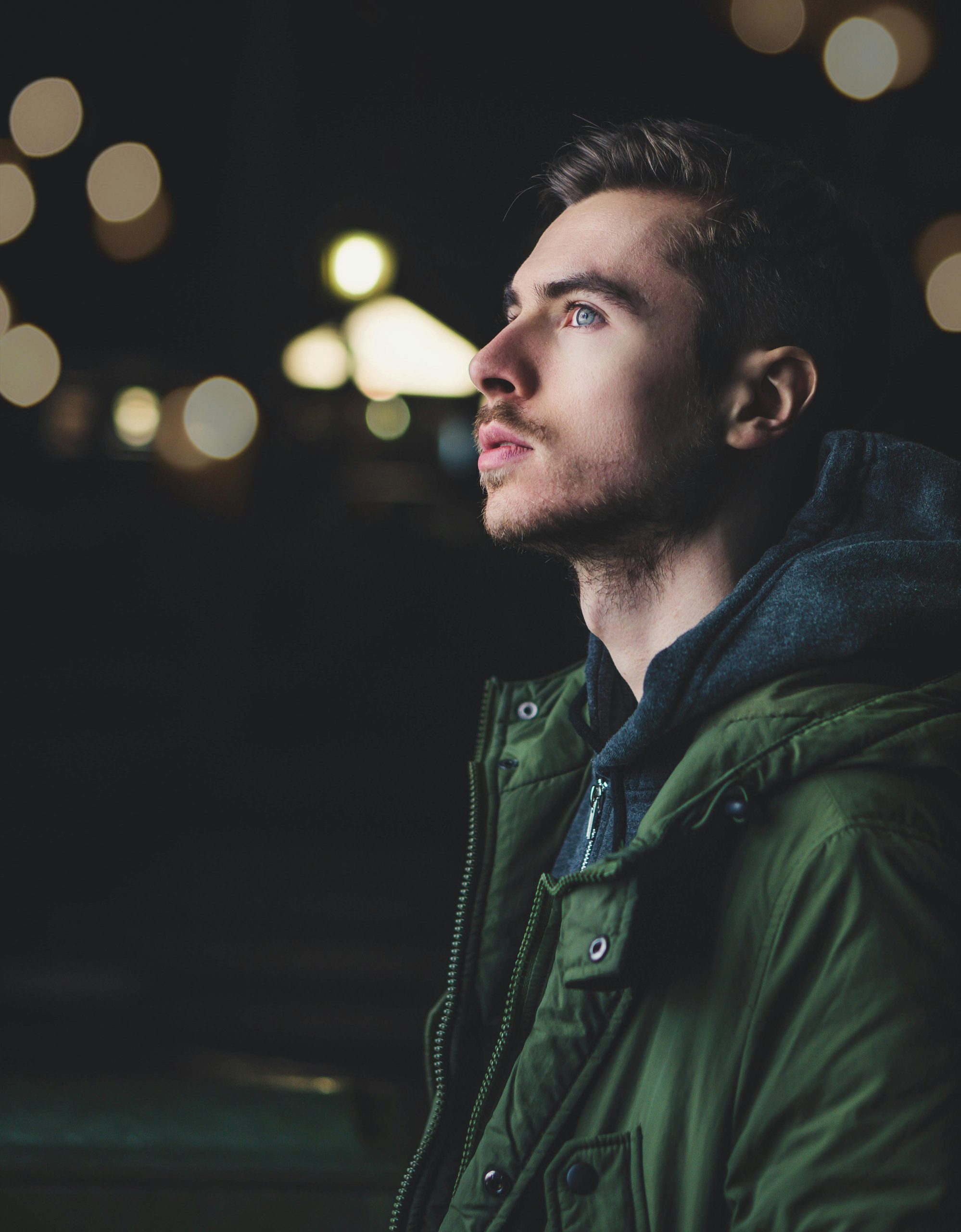 A young man in a jacket gazes thoughtfully upwards, illuminated by city lights.